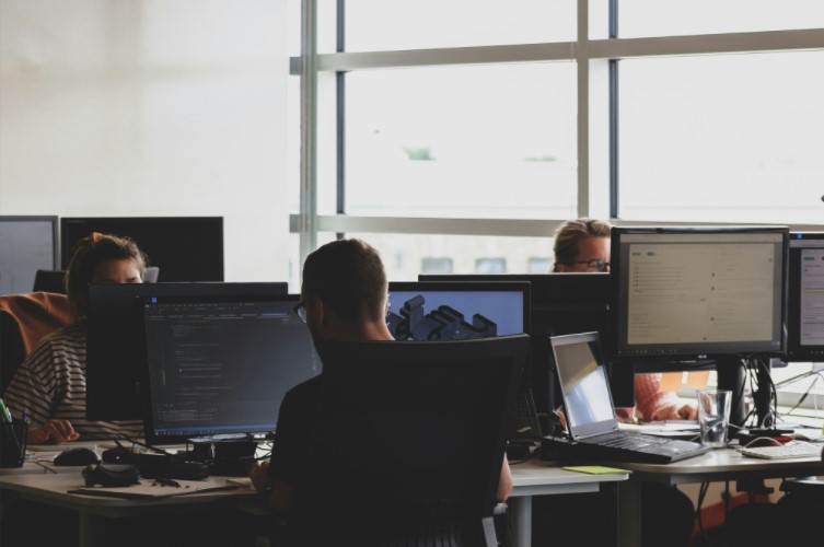 Equipe de funcionários trabalhando em escritório com computadores, ilustrando ambiente corporativo e saúde empresarial.